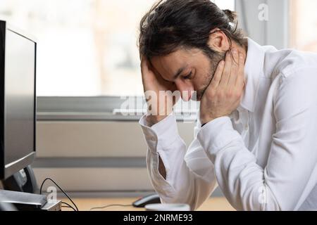portrait of a thinking young man. He is in the office at his workstation. Stock Photo