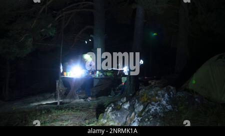 An abstract photo of the movement of a person at a tourist table in a campsite at night by a lantern in the forest next to a tent in Altai. Stock Photo