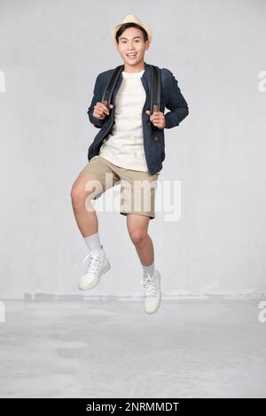Happy smiling young Asian tourist man with backpack jumping in mid-air Stock Photo