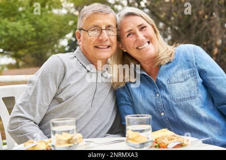 Portrait of happy elderly man and woman sitting with meal at table in garden of nursing home Stock Photo