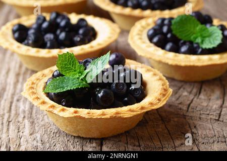 Bilberry, whortleberry or European blueberry with fresh green mint in mini tarts (tartlets) on rough rusric rural wooden table or background. Healthy Stock Photo
