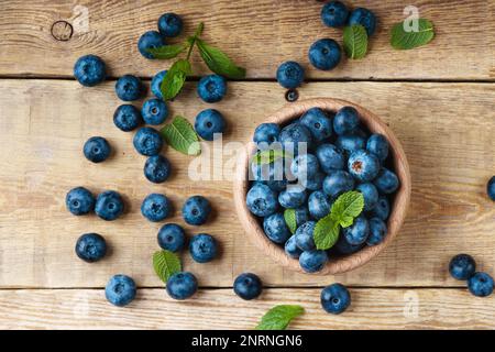 Freshly picked juicy and fresh blueberries with green mint leaves in light wooden bowl on rustic table. Bilberry on horizontal planks wooden backgroun Stock Photo