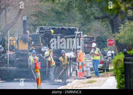 NEW ORLEANS, LA, USA - FEBRUARY 20, 2023: Workers spread hot, smoking asphalt on road surface behind heavy equipment during street repair project Stock Photo