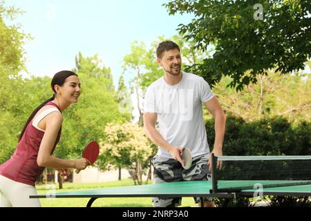 Happy couple playing ping pong in park Stock Photo