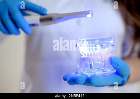 Photopolymer lamp Doctor Fairy with a glowing blue lamp in a white medical suit Dentist treatment of teeth prosthetics put fillings treat gums caries beautiful woman on white background studio ad Stock Photo