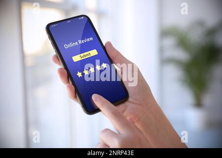 Woman using smartphone to give feedback indoors, closeup. Customer review Stock Photo