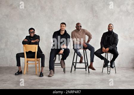 Young happy men against background of gray concrete wall. Multiethnic group of people. Fashion male models Stock Photo