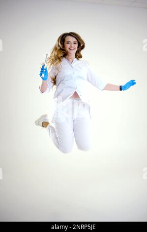 Photopolymer lamp Doctor Fairy with a glowing blue lamp in a white medical suit Dentist treatment of teeth prosthetics put fillings treat gums caries beautiful woman Jump up hover in the air studio ad Stock Photo