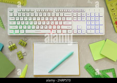 Modern keyboard with RGB lighting and stationery on grey marble table, flat lay Stock Photo