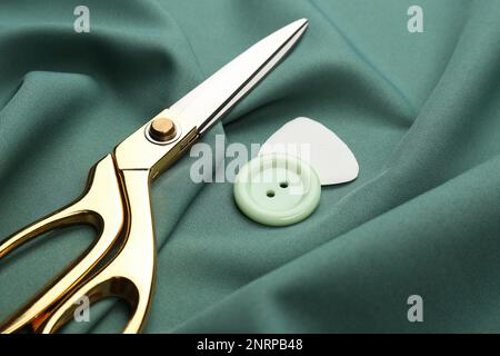 Scissors, button and tailor's chalk on green fabric, closeup Stock Photo