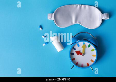 Sleeping mask, pills and alarm clock on light blue background, flat lay. Insomnia treatment Stock Photo