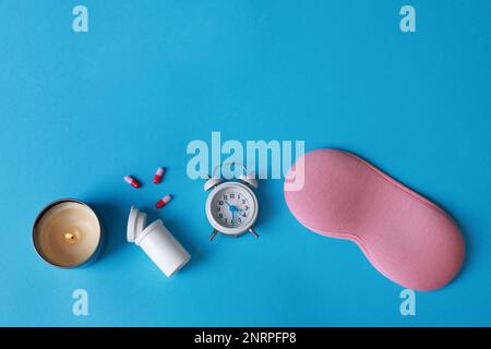 Sleeping mask, pills, candle and alarm clock on light blue background, flat lay. Insomnia treatment Stock Photo