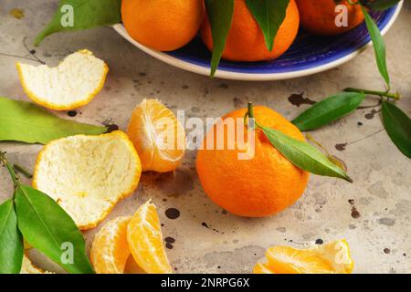 Tangerines (oranges, mandarins, clementines, citrus fruits) with leaves in blue plate on gray cement background. Organic vegetarian food. Winter local Stock Photo