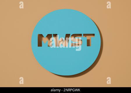 a blue paper sign with the german acronym MWST, for MehrwertSteuer, value-added tax, on a brown background Stock Photo