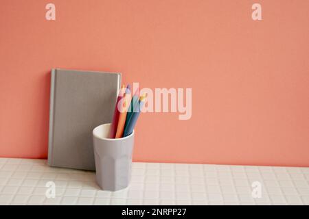Notebook and pen holder on white desk. pink wall background. workspace Stock Photo