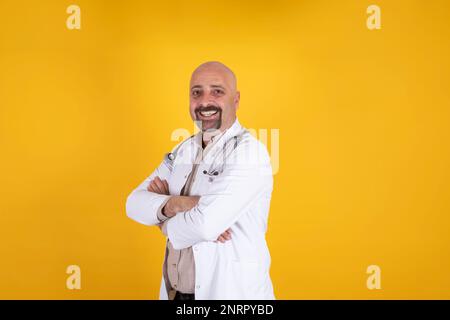 Portrait of confident smiling caucasian doctor. Male health care professional hospital worker posing over orange background. Crossing arms. Stock Photo
