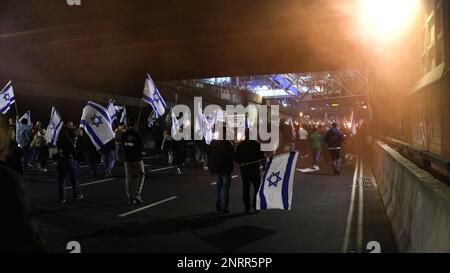 TEL AVIV, ISRAEL - FEBRUARY 25: Anti-government protesters hold Israeli flags and burning torches as they walk and block the Ayalon highway, one of the Israel's major freeways during a demonstration against Prime Minister Benjamin Netanyahu's new right-wing coalition and its proposed judicial changes that aims to weaken the country's Supreme Court on February 25, 2023 in Tel Aviv, Israel. Tens of thousands rally for eighth consecutive week across Israel against the wide ranging and controversial reform in Israel's legal system. Stock Photo