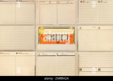 One vintage colorful orange compact cassette in front of tape boxes with empty labels Stock Photo