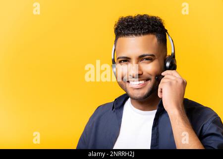 Smiling young indian man headset looking at the camera and smiles, positive man working in the customer service department in touch, isolated on yellow Stock Photo