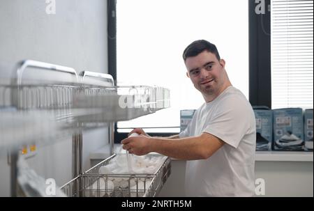 Young man with down syndome working in hospital as orderly. Concept of integration people with disability into society. Stock Photo