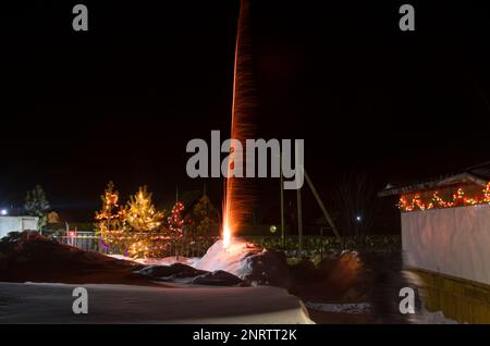 Bright flashes of fireworks in a garden plot in Siberia in winter with Christmas trees decorated with garlands on the snow at night. Stock Photo