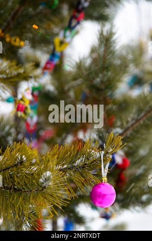 Multi-colored garlands and tinsel from the ball decorate the Christmas tree outdoors in the snow on New Year. Stock Photo