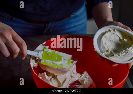 hands emptying the fresh white cheese from the packaging to mix it and prepare a cheesecake Stock Photo