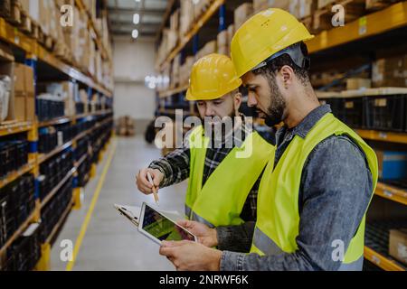 Warehouse workers checking stuff in warehouse with digital system in tablet. Stock Photo