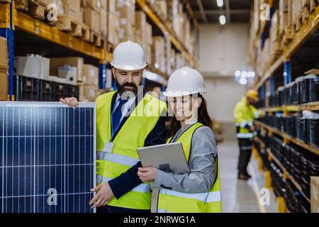 Warehouse workers checking stuff in warehouse with digital system in tablet, holding solar panel. Stock Photo