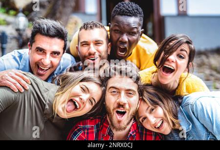 Multicultural men and women taking selfie outdoors on funny party mood - Mixed age range life style concept with young multiethnic hipster people havi Stock Photo