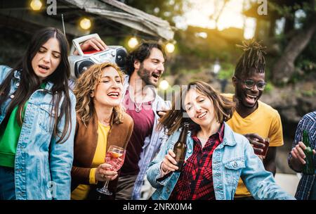 Multicultural friends group having fun out side cheering with drinks and beer bottles - Millenial people enjoying party at private villa together - Yo Stock Photo
