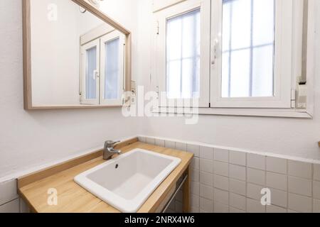 Small toilet with barred aluminum windows, wooden framed mirror and porcelain sink integrated into wooden countertop Stock Photo