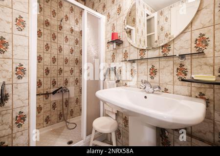 Antique bathroom with shower with sliding door screen, vintage tiles and white porcelain sink with mirror Stock Photo