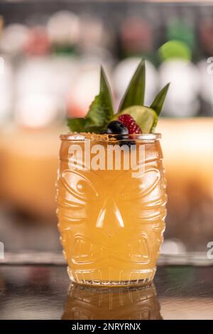 Mai Tai cocktail on the bar in the night club. Tiki rum drink garnished with pinneaple and blueberries on bar counter. Stock Photo