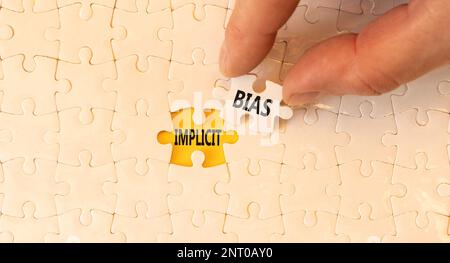 Implicit bias symbol. Concept words Implicit bias on white paper puzzles. Beautiful yellow table yellow background. Businessman hand. Business psychol Stock Photo