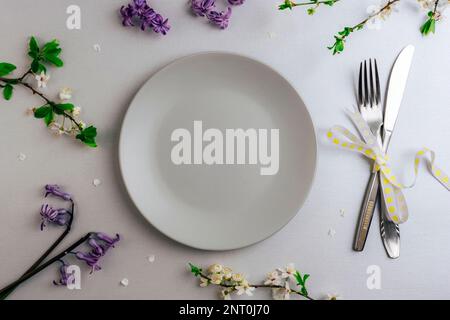 Spring table setting with gray plate, cherry blossom and blue hyacinth flowers on silver background. Top view, flat lay, copy space. Stock Photo