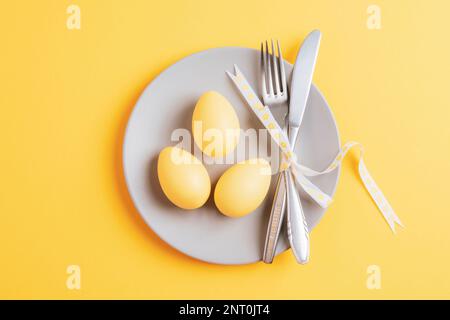 Gray plate with easter painted eggs on yellow background. Happy Easter card. Top view, flat lay. Stock Photo
