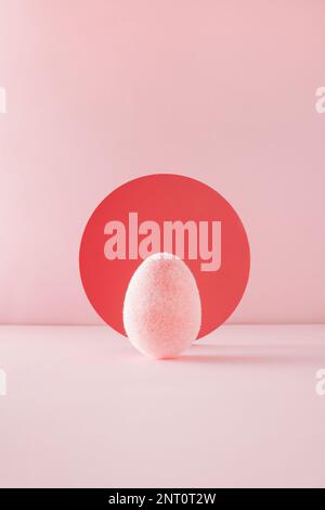 Soft fluffy pink egg in front of red circle backdrop on pink background. Minimal Easter concept. Stock Photo