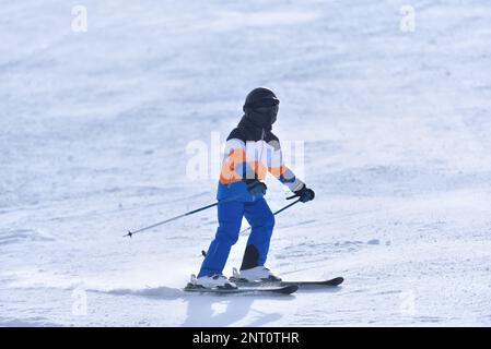 Speed and Adventure in the Sun: 10-Year-Old Boy Skiing Down a Sunny Slope with the Mountain in the Background Stock Photo