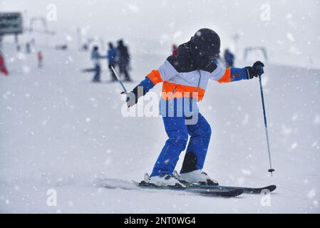 Speed and Adventure: 10-Year-Old Boy Skiing Down a Sunny Slope with the Mountain in the Background Stock Photo