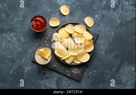 Plate with delicious potato chips, sauce, ketchup and sea salt on blue grunge background Stock Photo