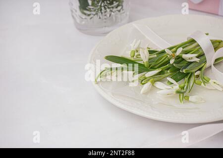 Plate with beautiful snowdrops and ribbon on white table Stock Photo