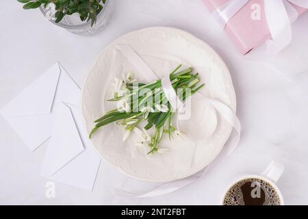 Plate with beautiful snowdrops and ribbon on white table Stock Photo