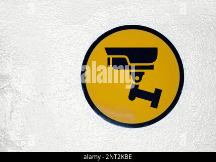 Close-up on a round black and yellow CCTV sign on a white wall. Stock Photo