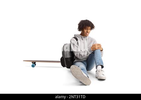 African american guy with a skateboard sitting on the ground and holding his injured knee isolated on white background Stock Photo