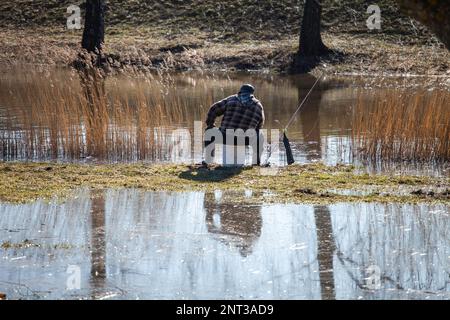 A lonely fisherman sitting on a bucket and fishing Stock Photo