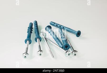 A group of construction screws with plastic dowels on a light background is reflected on a white mirror background Stock Photo