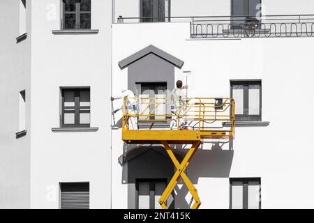 Two painters painting the facade of the building with paint rollers from the lift cradle Stock Photo