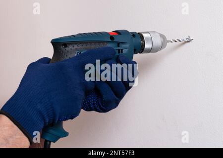 Electric drill in the hands of a man in gloves who drills a hole in the wall. Close up. Stock Photo