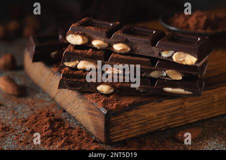 Dark and milk chocolate with nuts on a dark background sprinkled with cocoa powder. Chocolate pieces with almonds and hazelnuts close-up. Stock Photo